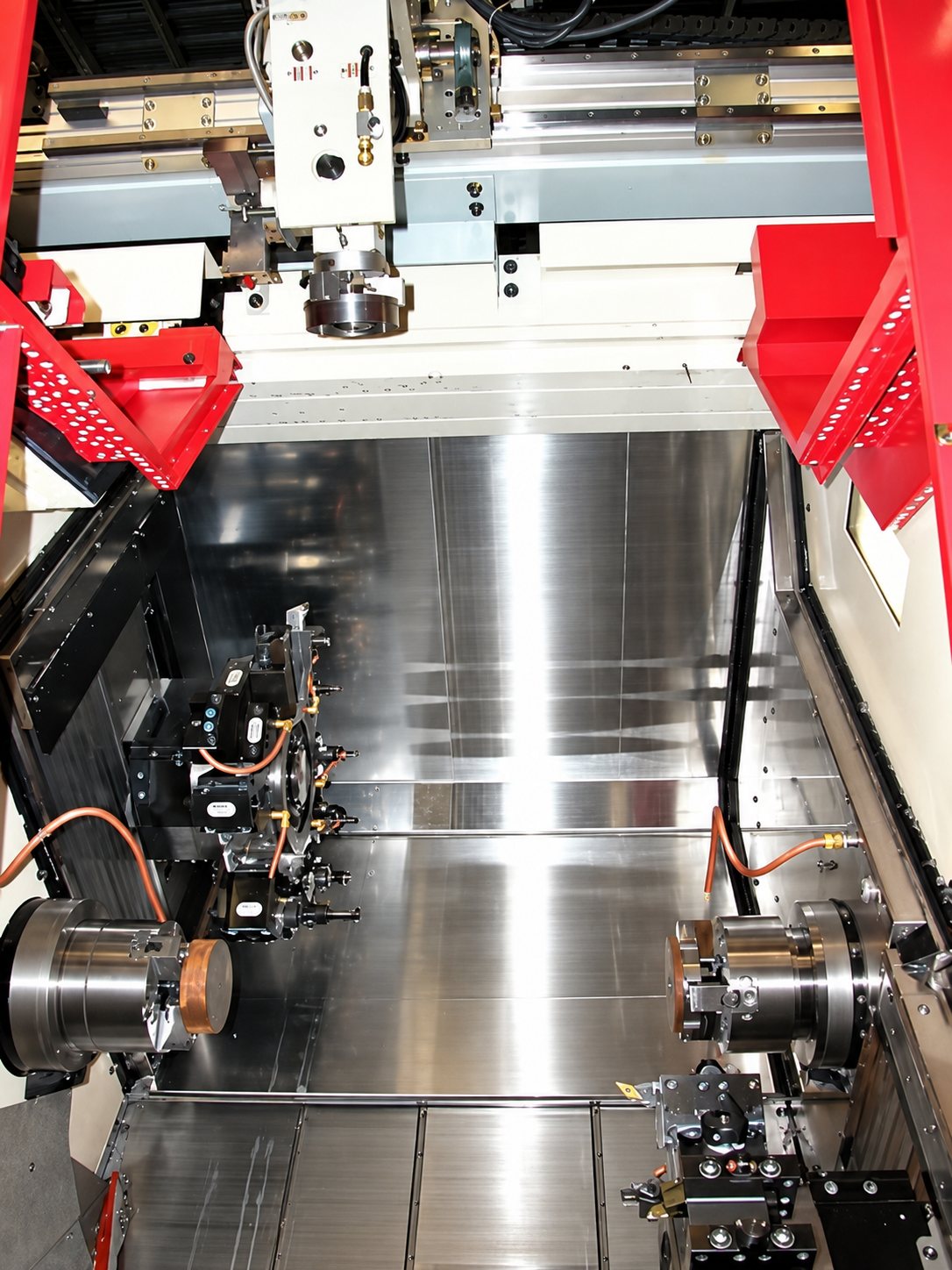 Vue de l'intérieur d'une machine-outil à commande numérique rouge et grise, avec deux broches, une tourelle d'outils et des parois en acier poli.