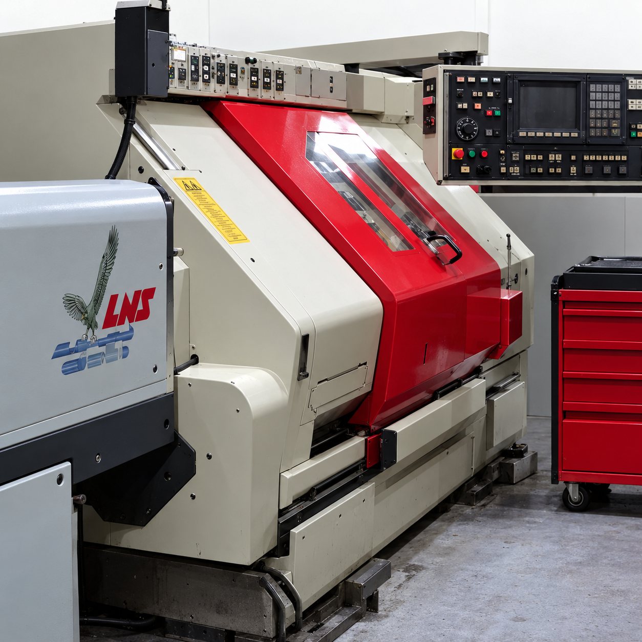 Une machine-outil à commande numérique rouge et blanche installée dans un atelier, avec un chariot d'outils rouge à droite.