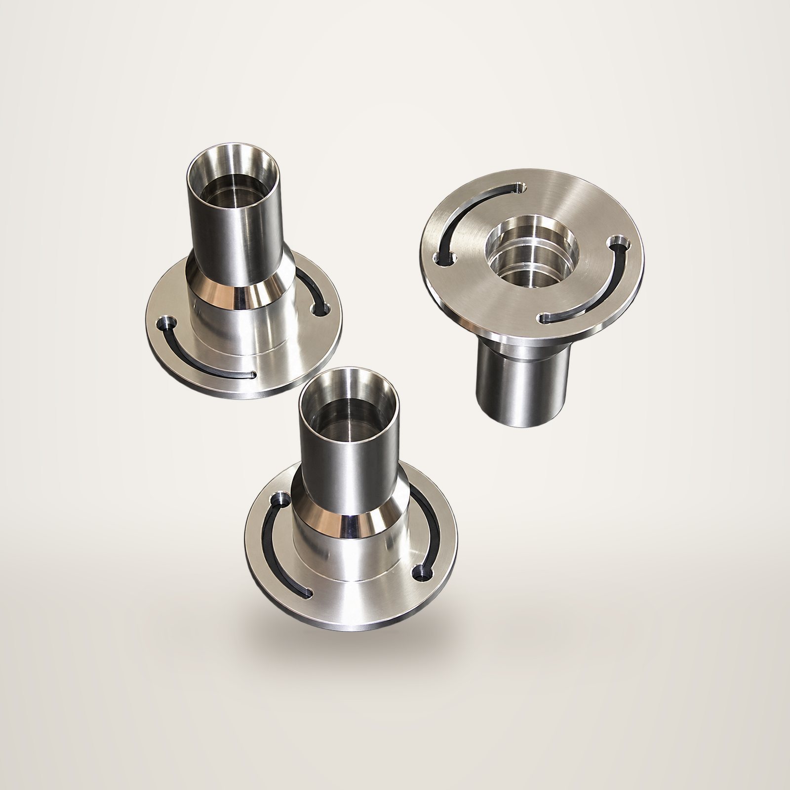 Trois pièces cylindriques en acier inoxydable poli, munies de brides circulaires percées de fentes courbes, posées sur une surface noire brillante.