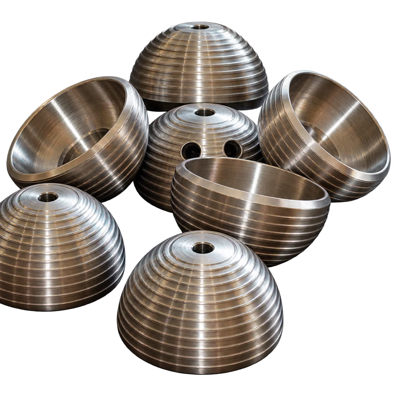 Plusieurs demi-sphères métalliques dorées aux rainures concentriques, posées sur un fond blanc uni.