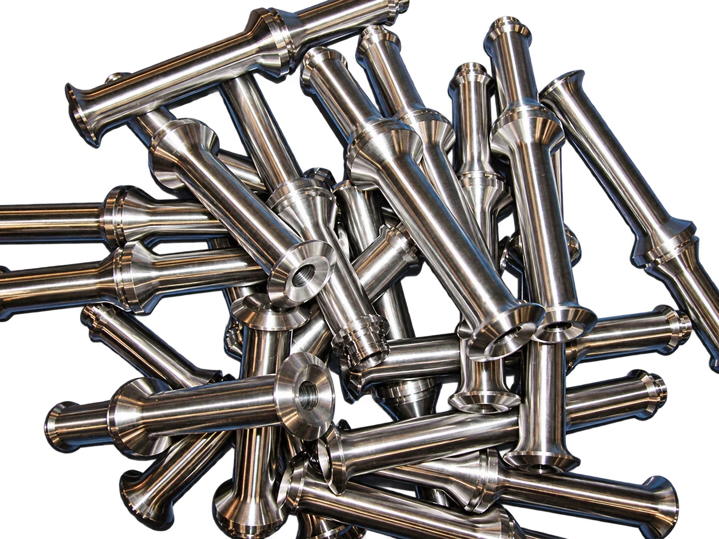 Un tas de pièces cylindriques en acier inoxydable poli, usinées avec précision, posées sur une surface bleue.