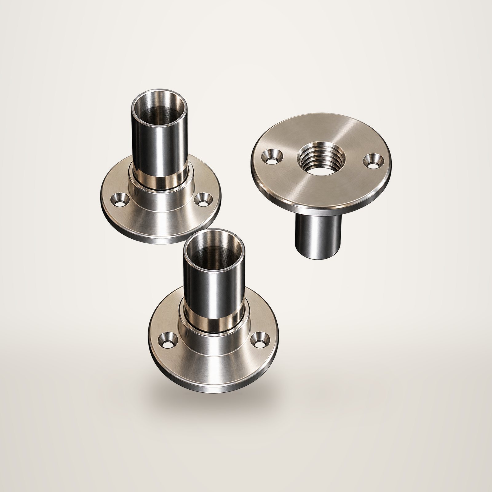 Trois pièces cylindriques en acier inoxydable poli avec collerette, posées sur un fond blanc uni.
