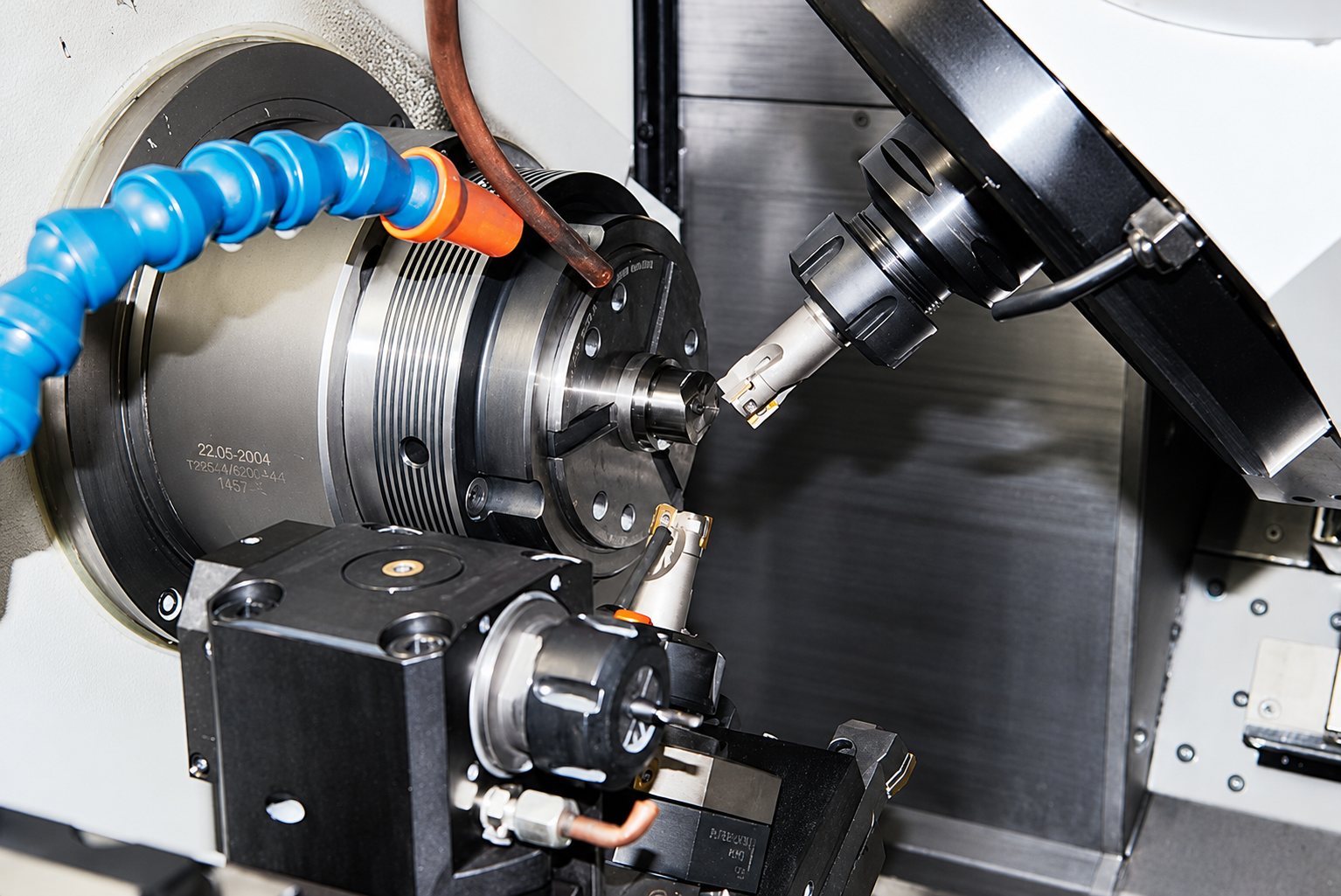 Gros plan sur l'intérieur d'une machine-outil CNC où un outil de fraisage usine une petite pièce métallique serrée dans la broche, avec un tuyau d'arrosage bleu.
